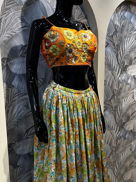 Orange silk blouse with handmade floral and mirror embroidery, paired with full-length multicolored printed skirt